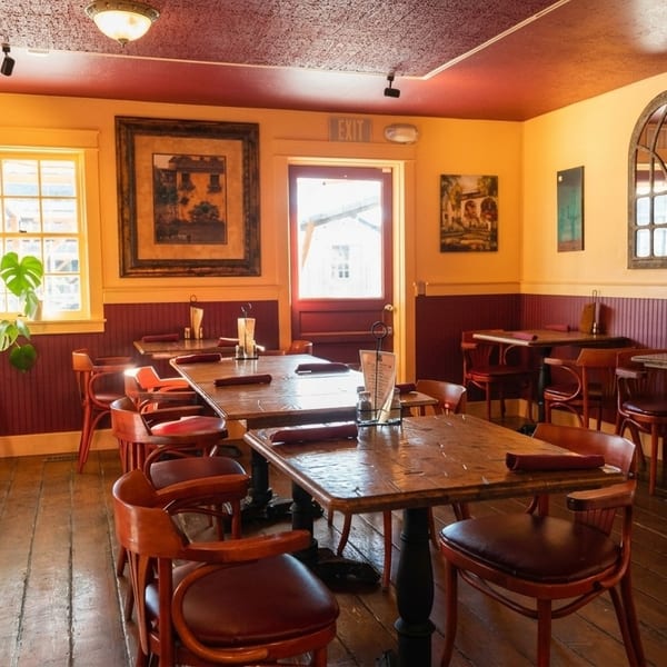 Cozy restaurant interior with wooden tables and chairs, yellow walls, and red wainscoting.