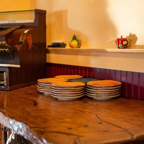 Vintage wooden cash register and stacks of plates on a rustic wooden counter with red wainscoting.