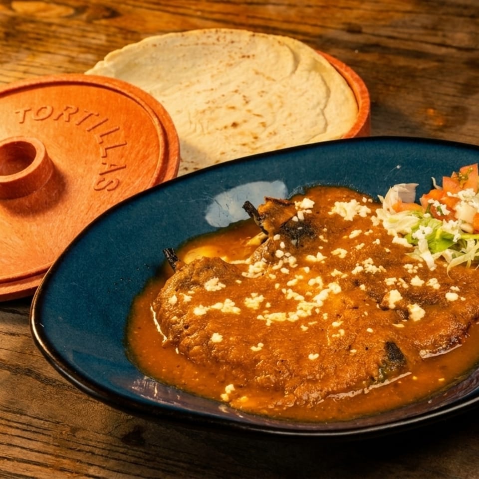 Chiles Rellenos in a blue dish with a side of tortillas and a terracotta tortilla warmer.