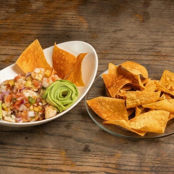 Ceviche with avocado, lime, and tortilla chips on a rustic wooden table.