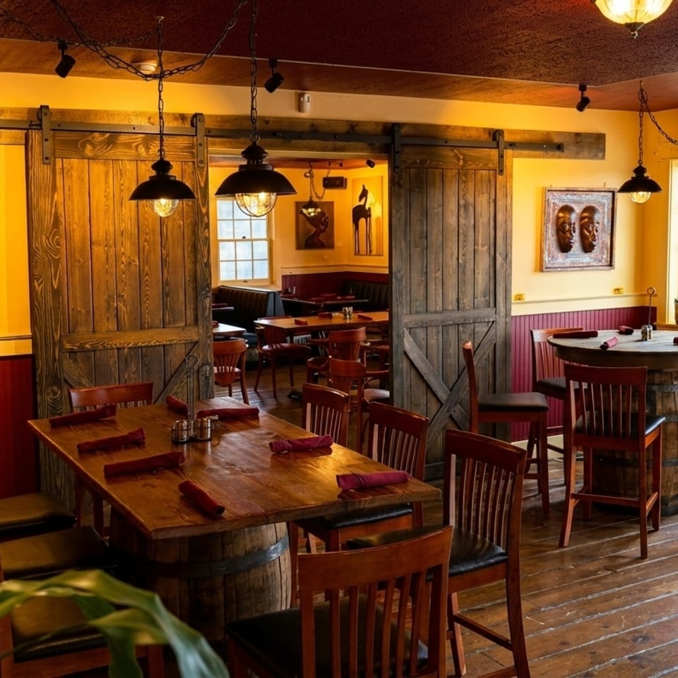 Warm, rustic restaurant interior with wooden tables, red wainscoting, and barn doors leading to another dining area.